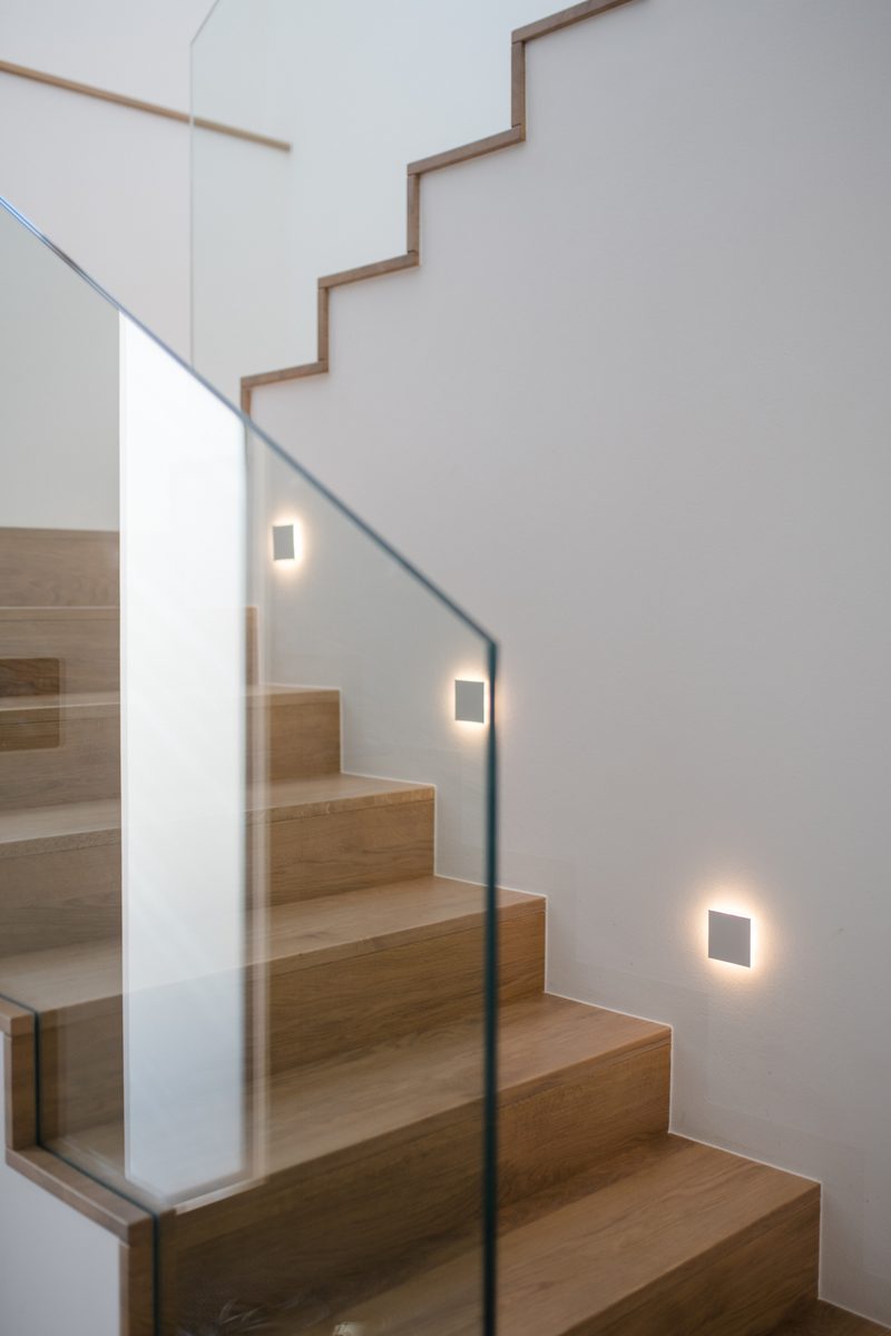 Detailaufnahme einer Holztreppe mit Glasgeländer und in die Wand eingelassenen Stufenleuchten