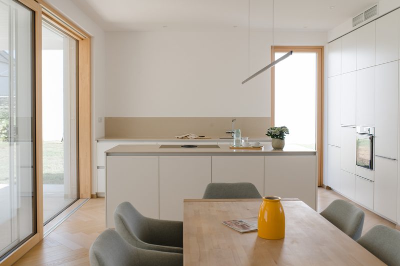 Offene Küche mit heller Kochinsel, raumhoher Schiebetür zum Garten und Fischgrätparkett