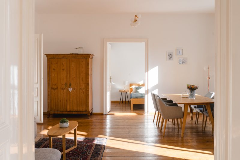 Lichtdurchfluteter Wohnraum mit antikem Holzkleiderschrank, Esstisch und Blick ins Schlafzimmer