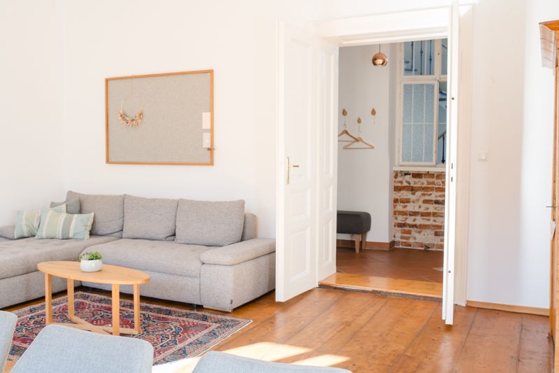 Wohnzimmer mit Sofa und Blick durch eine offene Tür auf einen Flur mit Ziegelwand